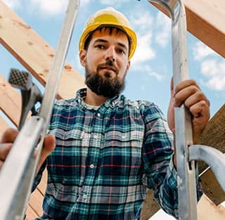 A man in a hard hat and plaid shirt stands on a ladder, representing Titan Exteriors. A man in a hard hat and plaid shirt stands on a ladder, representing Titan Exteriors.