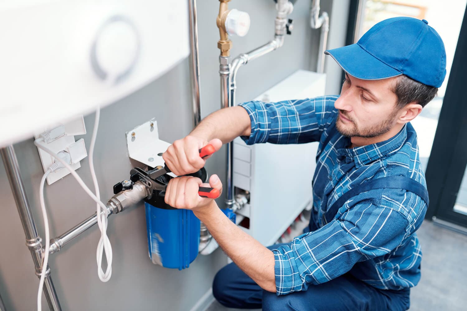 A man in blue overalls repairs a water heater, representing Titan Exteriors' plumbing services. A man in blue overalls repairs a water heater, representing Titan Exteriors' plumbing services.